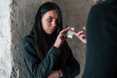 Two people standing with illegal drugs in little package indoorsの写真素材