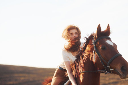 Young woman in protective hat with her horse in agriculture field at sunny daytimeの写真素材
