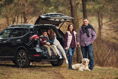 Happy family have fun with their dog near modern car outdoors in forestの写真素材
