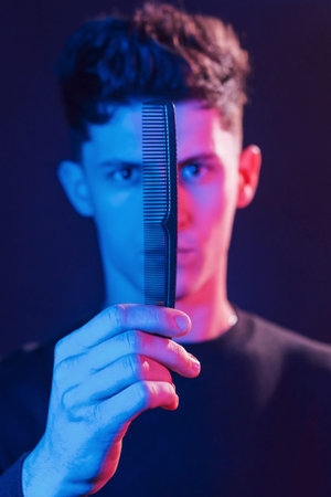 Young barber with work equipment standing in the studio with neon lighting