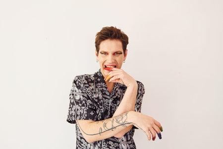 Young gay man is standing in the studio and posing for a camera. Multicolored make up on face fingersの写真素材