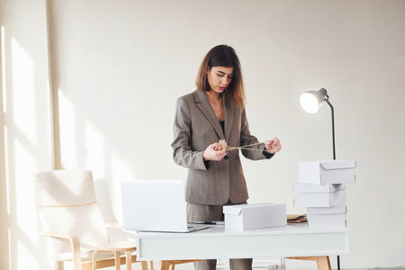 Packaging orders into the white boxes. Young woman in formal clothes is indoors. Conception of styleの写真素材