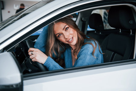 Positive woman in blue shirt sits inside of new brand new car. In auto salon or airportの写真素材
