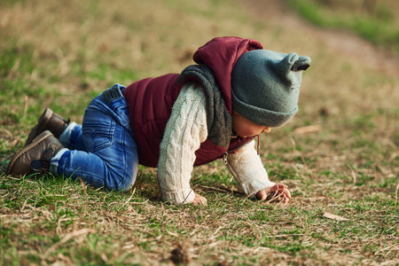 Little boy in warm clothes lying down on ground of field on grassの写真素材