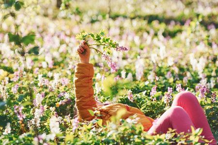 Happy little girl in casual clothes lying down on ground in spring forest at daytimeの写真素材