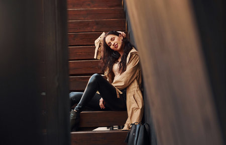 Cheerful brunette in black leggings sitting on wooden stairs and smilingの写真素材