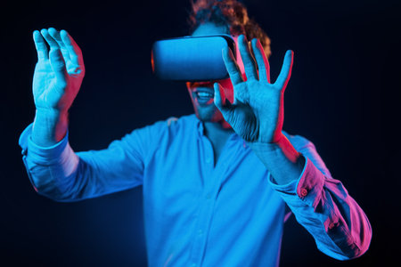 Virtual glasses gaming experience. Neon lighting. Young european man is in the dark studioの写真素材