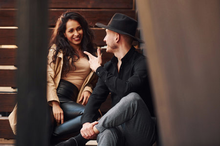 Cheerful brunette in black leggings sitting on wooden stairs with her man in hatの写真素材