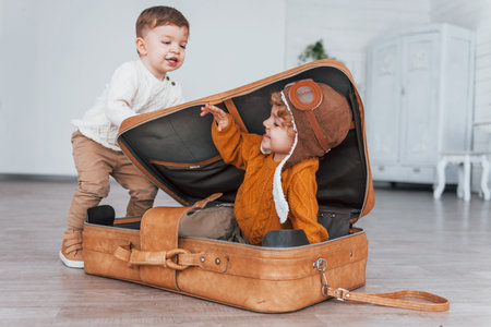 Two little boys have fun and sitting in suitcase indoors at daytimeの写真素材