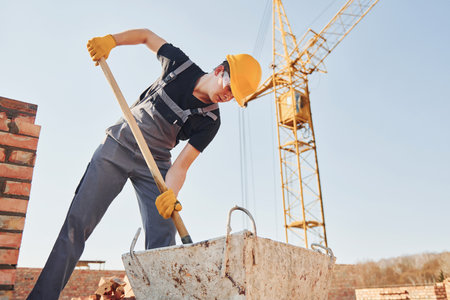 Using showel. Construction worker in uniform and safety equipment have job on buildingの写真素材