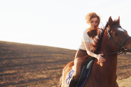 Young woman in protective hat with her horse in agriculture field at sunny daytimeの写真素材