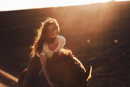 Young woman in protective hat with her horse in agriculture field at sunny daytimeの写真素材