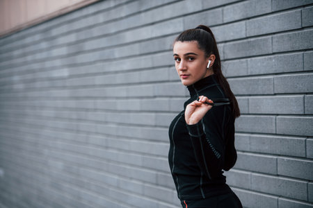 Young sportive girl in black sportswear standing with jump rope in hands outdoors near gray wallの写真素材