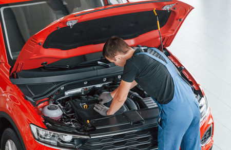Top view of male worker in uniform that repairs red automobileの写真素材