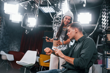 Young man is preparing for TV online broadcast. Woman helps with make up