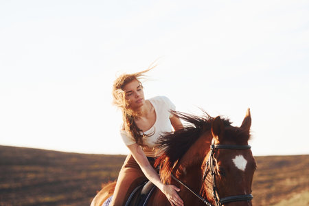 Young woman in protective hat with her horse in agriculture field at sunny daytimeの写真素材