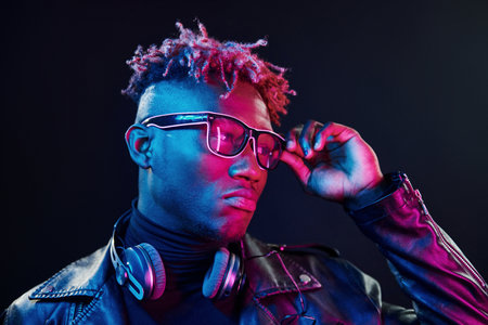 Stylish glasses and wireless headphones. Futuristic neon lighting. Young african american man in the studioの写真素材