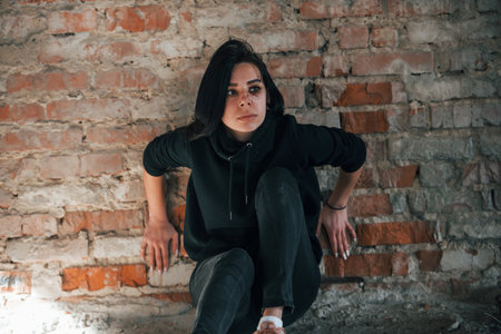 Young beaten woman in black clothes sitting on the floor of abandoned buildingの写真素材