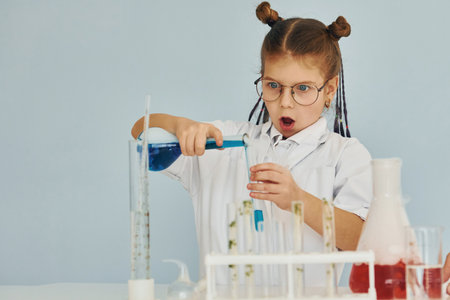 Little girl in coat playing a scientist in lab by using equipmentの写真素材