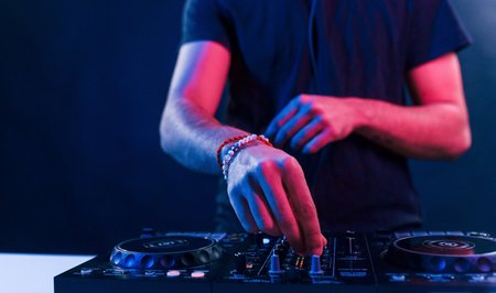 Close up view of DJs hands that working with music equipment in the club with neon lightingの写真素材