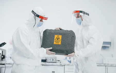 With biological hazard case. Female medical workers in protective uniform works on COVID-19 vaccineの写真素材