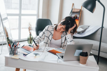 With laptop on the table. Young female freelance worker is indoors in home at daytimeの写真素材
