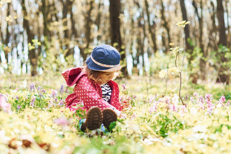 Happy little girl in blue hat have walk in spring forest at daytimeの写真素材
