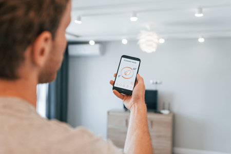 Holds phone. Rear view of adult man that is indoors controlling smart home technologyの写真素材