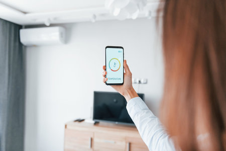 Rear view of woman that is indoors controlling smart home technologyの写真素材