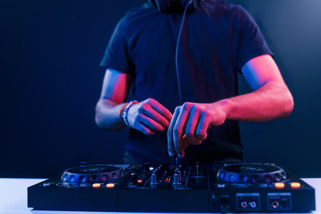 Close up view of DJs hands that working with music equipment in the club with neon lightingの写真素材