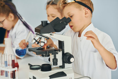 Using microscope. Children in white coats plays a scientists in lab by using equipmentの写真素材