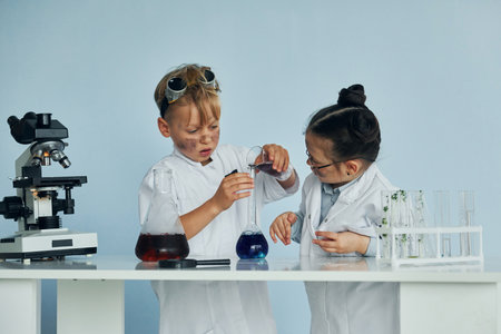 Little girl and boy in white coats plays a scientists in lab by using equipmentの写真素材