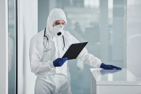 Male doctor scientist in lab coat, defensive eyewear and mask holding notepad in handsの写真素材