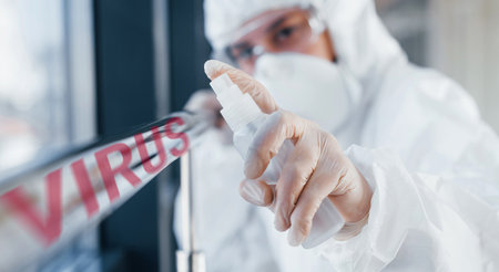 Red virus word. Nurse in protective uniform, mask and glasses standing indoorsの写真素材