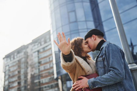 Cheerful couple in casual warm clothes kissing outdoors in the city near business buildingの写真素材