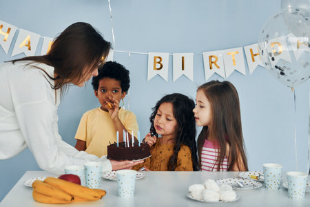 Woman holds cake. Children on celebrating birthday party indoors have fun togetherの写真素材