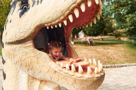 Cheerful little girl having fun in park with dinosaur replicas outdoorsの写真素材