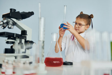 Little girl in coat playing a scientist in lab by using equipmentの写真素材