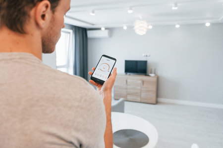 Holds phone. Rear view of adult man that is indoors controlling smart home technologyの写真素材