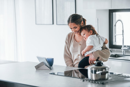 Female blogger mother with her kid together indoors at home at weekend using tabletの写真素材
