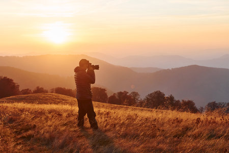 Male photographer standing and working at majestic landscape of autumn trees and mountains by the horizonの写真素材