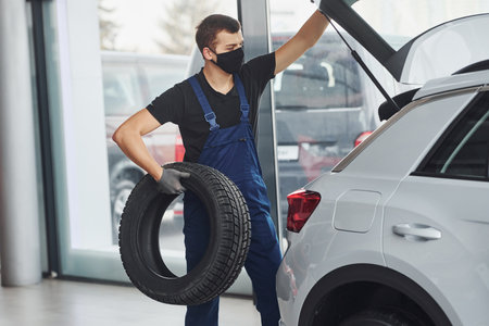 Worker in black and blue uniform holding car wheel and have job indoorsの写真素材