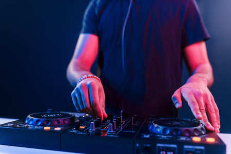 Close up view of DJs hands that working with music equipment in the club with neon lightingの写真素材