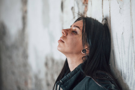 Portrait of beaten young woman with bruise under eye that standing and leaning on the wall indoors in abandoned buildingの写真素材