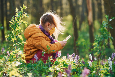 Happy little girl in protective mask sitting in spring forest at daytimeの写真素材