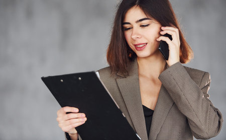 Talks by phone. Young woman in formal clothes is indoors. Conception of styleの写真素材