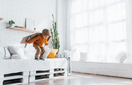 Little boy in retro pilot uniform running with toy plane indoorsの写真素材