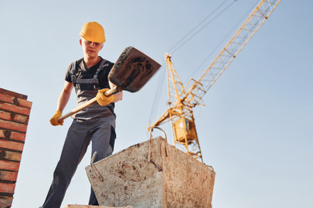 Using showel. Construction worker in uniform and safety equipment have job on buildingの写真素材