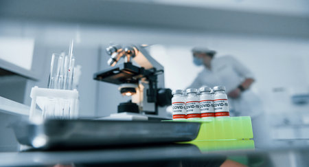 Using microscope. Female medical workers in protective uniform works on COVID-19 vaccineの写真素材