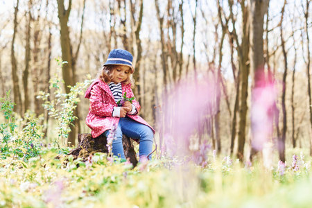 Happy little girl in blue hat have walk in spring forest at daytimeの写真素材